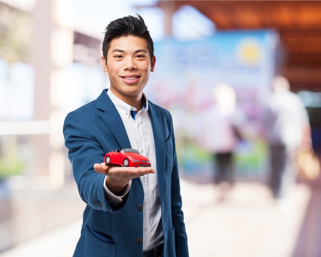 Hombre sonriendo mientras sostiene un coche rojo de juguete