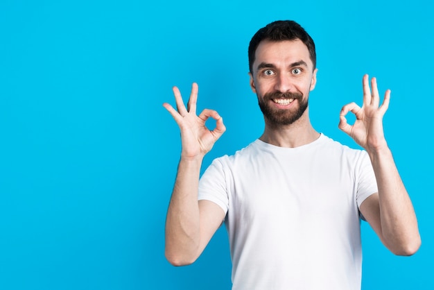 Hombre sonriendo y posando mientras sostiene el signo bien