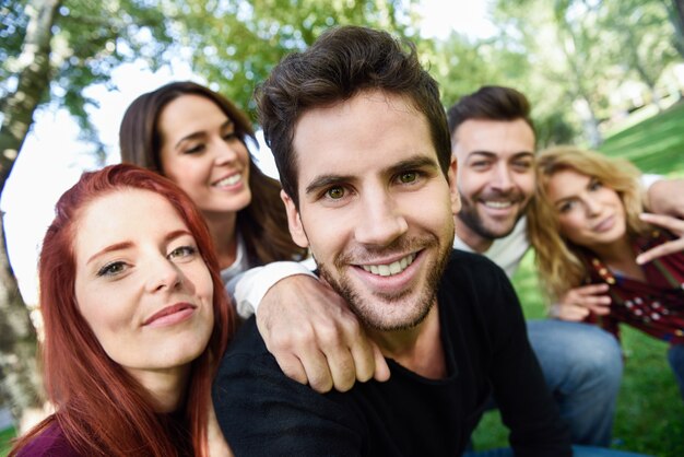 Hombre sonriendo tomando una auto foto de el y sus amigos con árboles de fondo