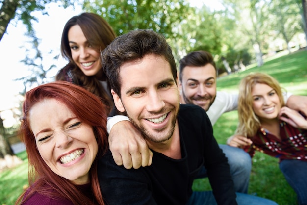 Hombre sonriendo tomando una auto foto de el y sus amigos con un parque de fondo