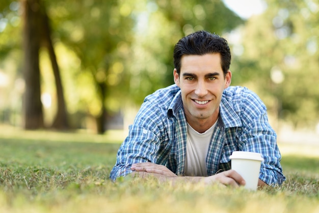 Hombre sonriendo tumbado en el césped con un café