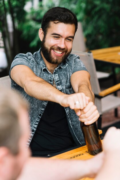 Hombre sonriente abriendo la botella de alcohol sentado en el restaurante