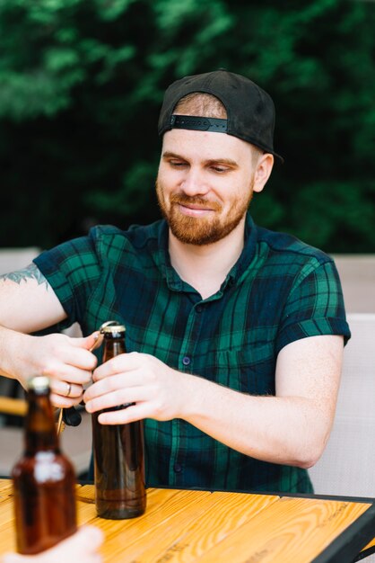 Hombre sonriente abriendo la tapa de la botella con el abrelatas en la mesa de madera