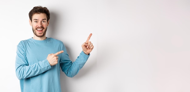 Foto gratuita hombre sonriente alegre señalando con el dedo a la derecha y mostrando pancarta o logotipo en un espacio en blanco para publicidad