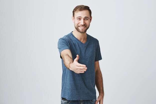 Hombre sonriente amable estirar la mano hacia adelante para un apretón de manos, saludo