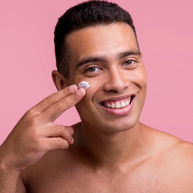Hombre sonriente aplicando crema en el rostro
