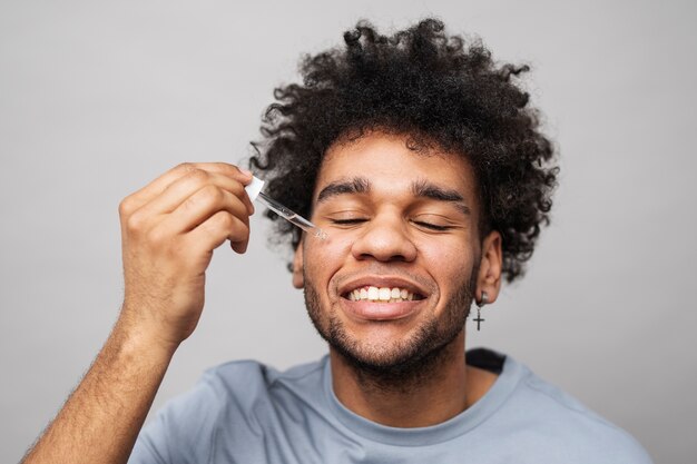 Hombre sonriente aplicando suero facial