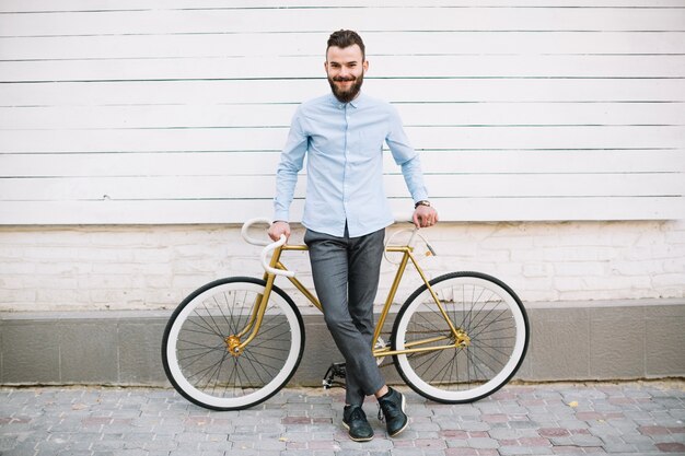 Hombre sonriente apoyado en bicicleta junto a la pared