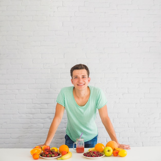 Hombre sonriente apoyado en el escritorio con muchas frutas coloridas