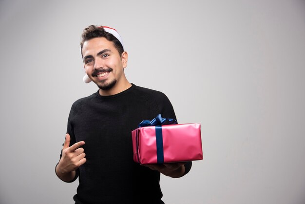 Hombre sonriente apuntando a una caja de regalo sobre una pared gris.