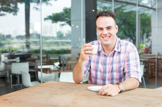 Hombre sonriente bebiendo café en el café al aire libre