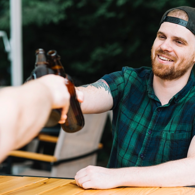 Hombre sonriente brindando botellas de cerveza con su amigo