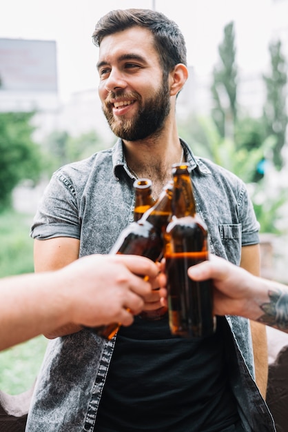 Hombre sonriente brindando botellas de cerveza con su amigo