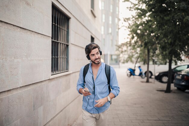 Hombre sonriente caminando sobre el pavimento escuchando música