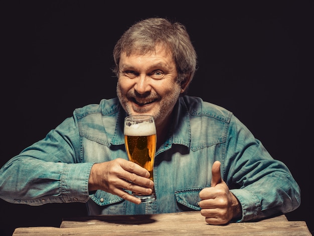 hombre sonriente en camisa vaquera con vaso de cerveza