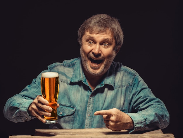 El hombre sonriente en camisa vaquera con vaso de cerveza