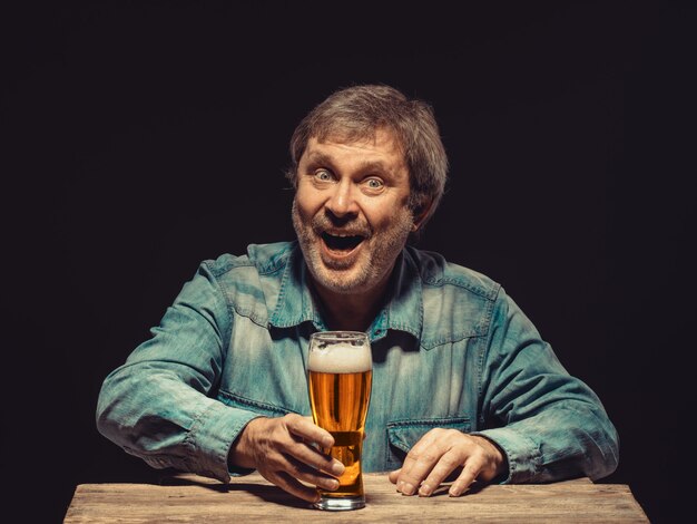 El hombre sonriente en camisa vaquera con vaso de cerveza