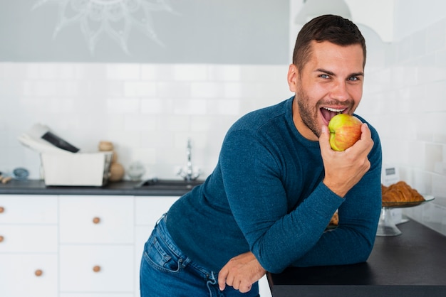 Hombre sonriente en casa comiendo manzana