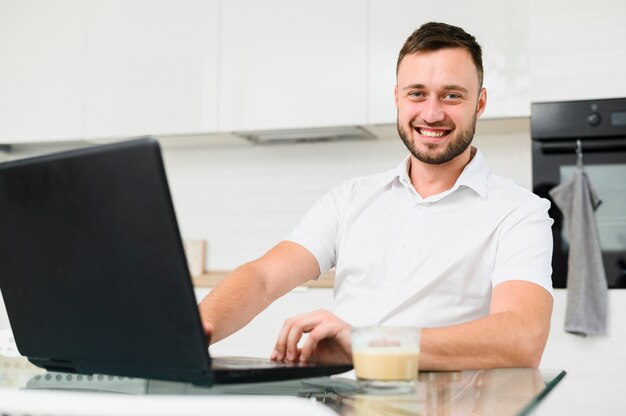 Hombre sonriente en cocina con laptop en frente