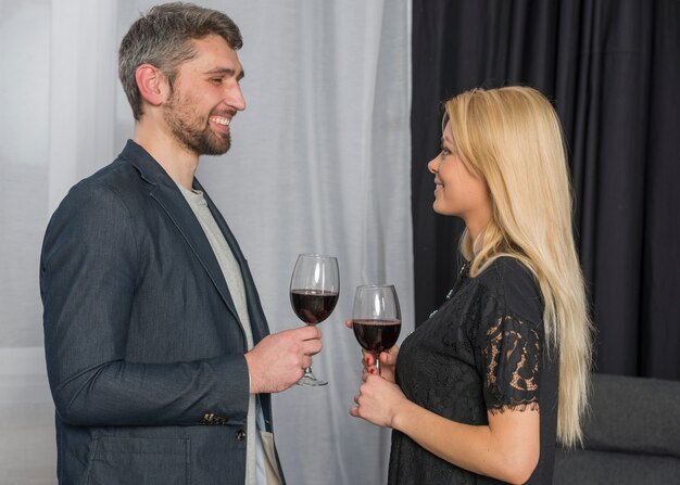 Hombre sonriente con copas de vino cerca de mujer alegre