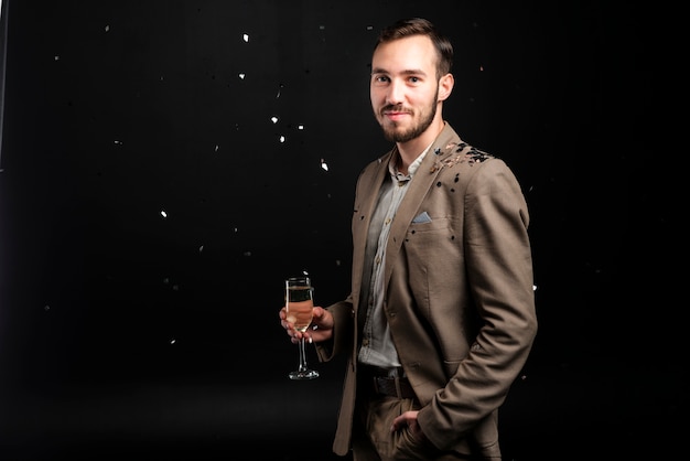 Hombre sonriente cubierto de confeti con copa de champán