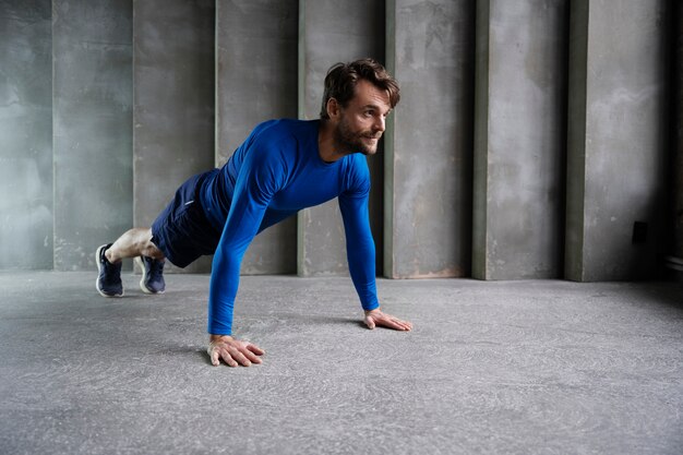 Hombre sonriente deportivo de tiro completo haciendo ejercicio en interiores