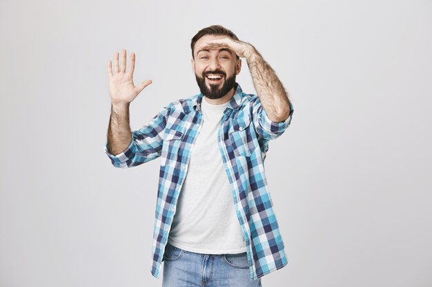 Hombre sonriente emocionado mirando a distancia, saludando a alguien, saludando con la mano hola