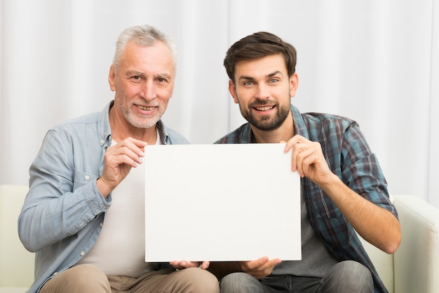 Hombre sonriente envejecido e individuo feliz joven que sostiene el papel en el sofá