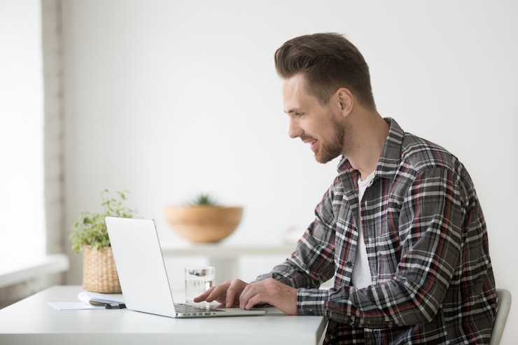 Foto gratuito hombre sonriente freelance trabajando en una computadora portátil comunicándose en línea usando software
