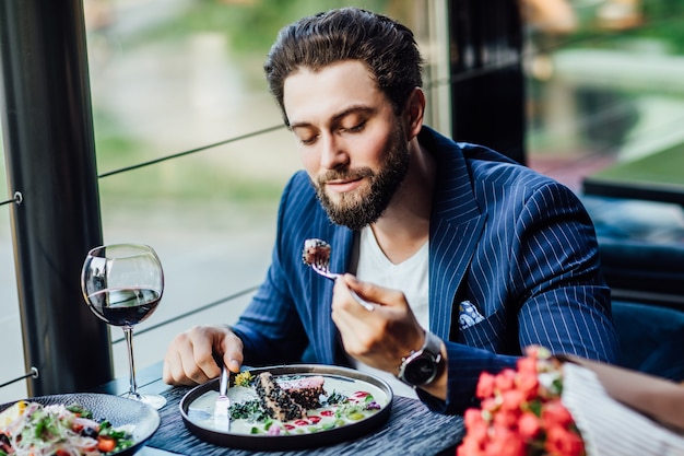 Hombre sonriente guapo comer ensalada en restaurante y mujer esperando con ramo de rosas