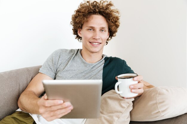 Hombre sonriente guapo sentado en el sofá con tablet PC