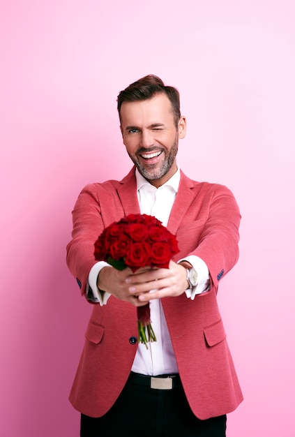 Foto gratuita hombre sonriente guiñando un ojo y dando ramo de rosas