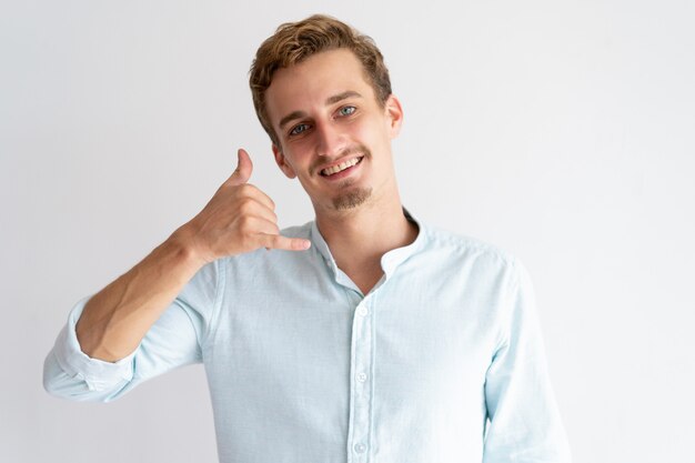 Hombre sonriente haciendo llamarme gesto y mirando a cámara