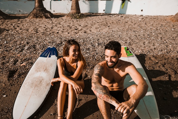 Foto gratuita hombre sonriente joven cerca de tablas alegres de la mujer y de resaca en orilla