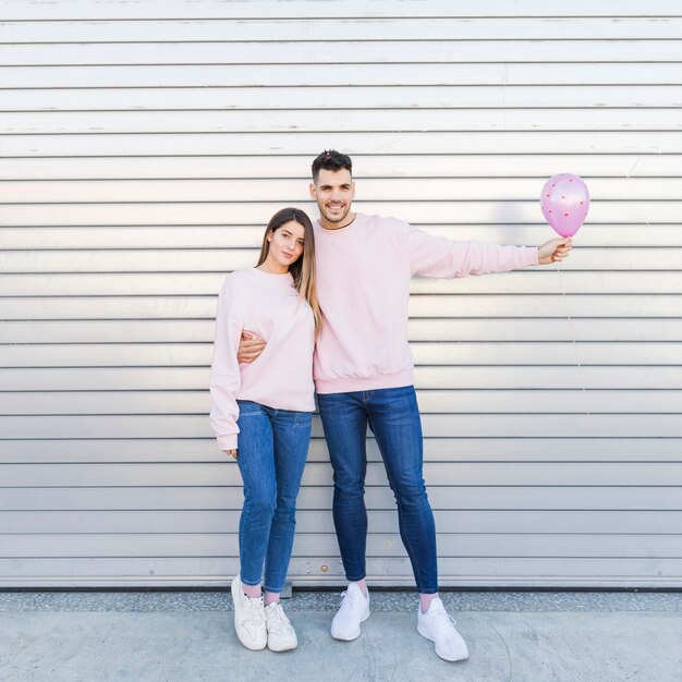 Hombre sonriente joven con el globo que abraza a la mujer atractiva