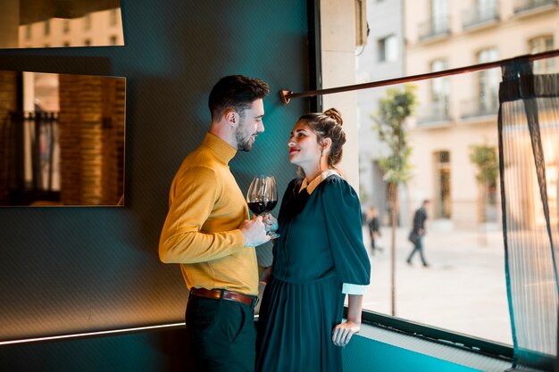 Hombre sonriente joven y mujer feliz con los vidrios de vino cerca de la ventana