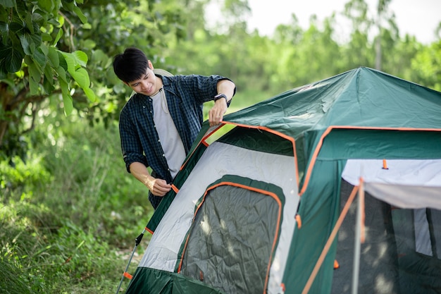 Hombre sonriente joven viajero colocando una carpa en el camping en el bosque en vacaciones de verano