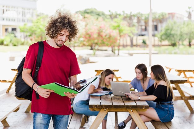 Hombre sonriente leyendo libros de texto cerca de amigos