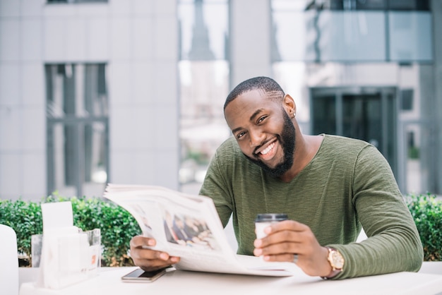 Hombre sonriente leyendo periódico en café