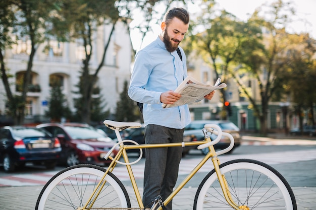 Hombre sonriente leyendo periódico cerca de bicicleta