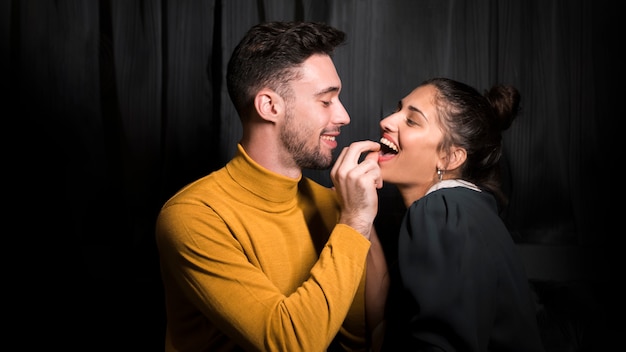 Hombre sonriente con la mano cerca de boca abierta de mujer alegre