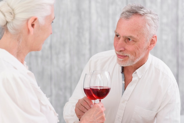 Hombre sonriente mayor que hace clic la copa de vino mientras que mira a su esposa