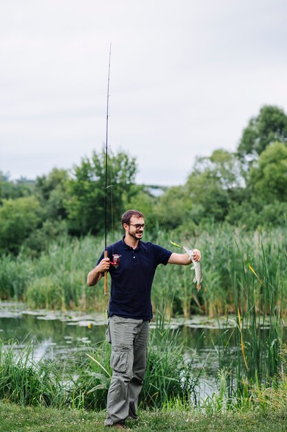 Hombre sonriente mirando peces recién capturados cerca del lago