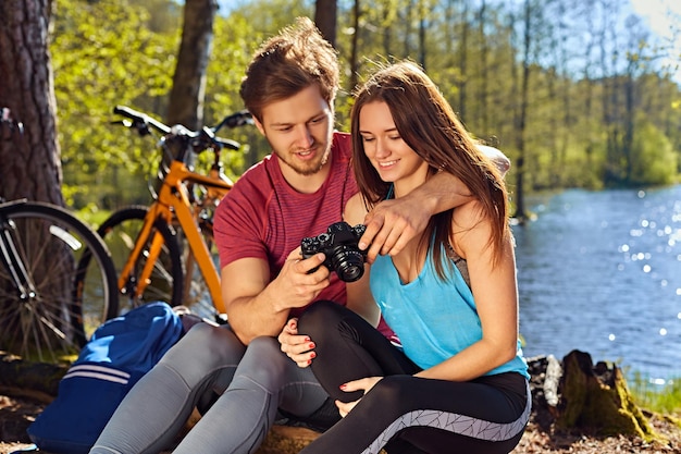 Hombre sonriente mostrando fotos de paseos en bicicleta a su novia en la costa salvaje del río.