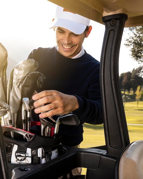 Foto gratuita hombre sonriente poniendo palos en carrito de golf