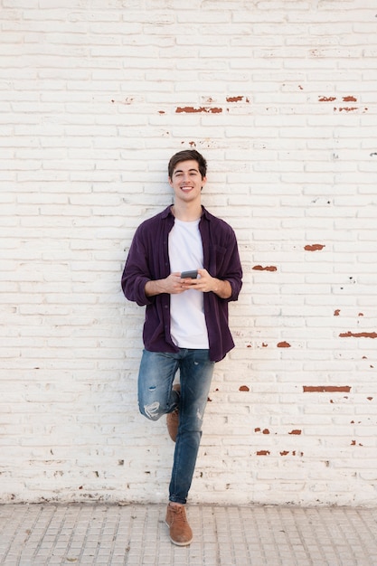 Hombre sonriente posando mientras sostiene el teléfono inteligente