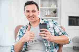 Foto gratuita hombre sonriente con el pulgar hacia arriba sosteniendo la taza de bebida en silla en casa