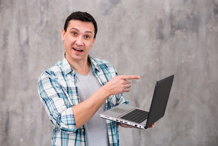 Foto gratuito hombre sonriente que se coloca con la computadora portátil y que señala en la pantalla