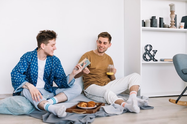 Hombre sonriente que da el libro a su amigo que sostiene el tarro de jugo en la mano