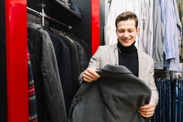 Hombre sonriente que elige la chaqueta en una tienda